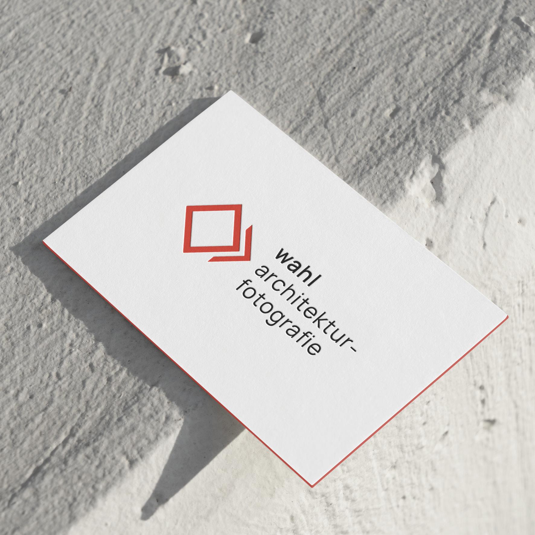 Eine weiße Visitenkarte mit einem roten quadratischen Logo und dem Schriftzug „wahl architektur-fotografie“ in schwarzen Kleinbuchstaben, platziert auf einer strukturierten weißen Oberfläche.
